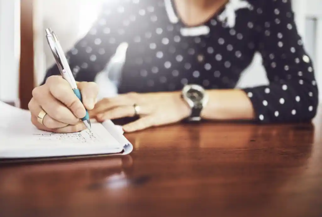 person with pen and book making a list